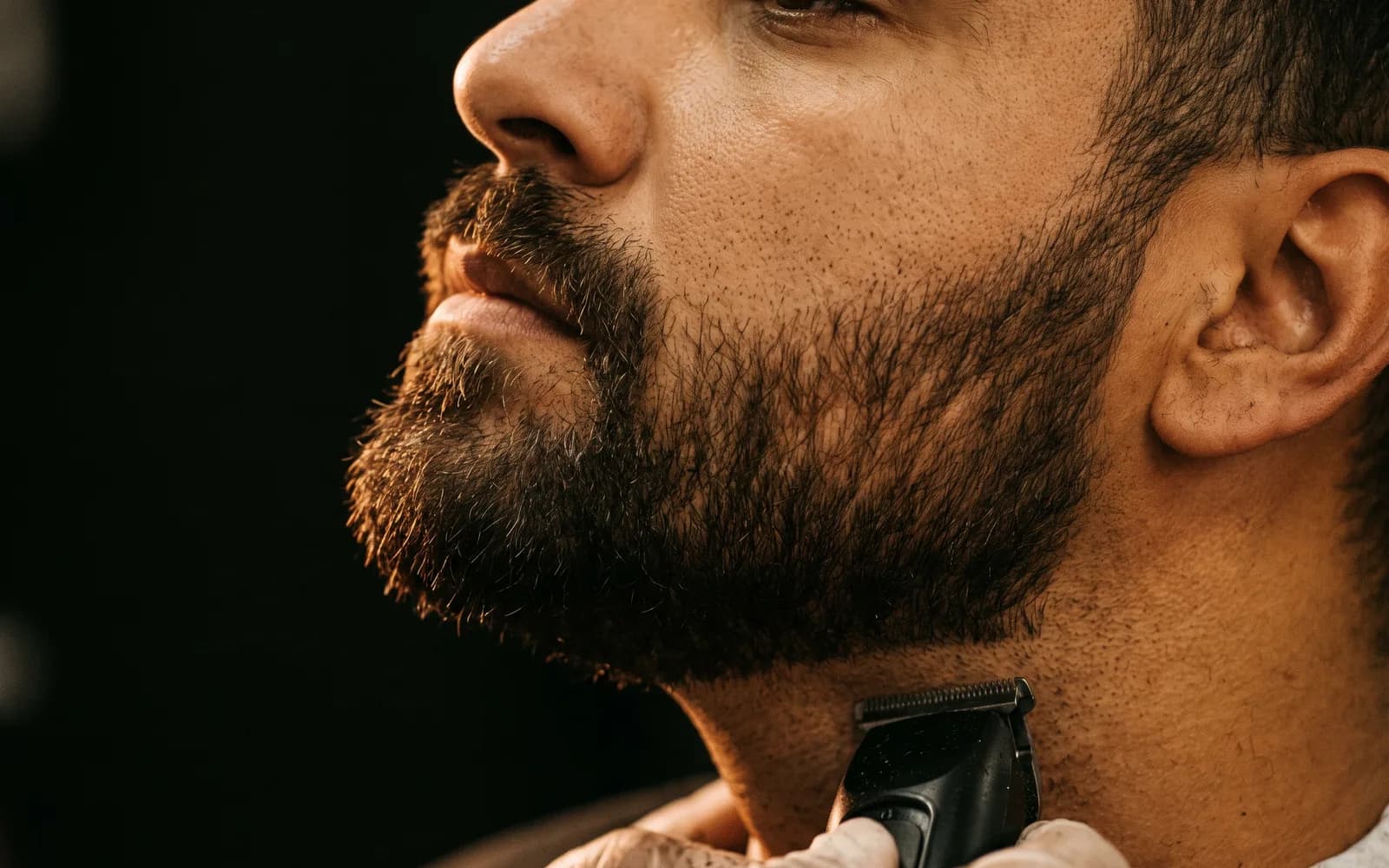 Contorno da barba sendo desenhado com máquina na linha do pescoço, em close de perfil. Imagem ilustrativa.