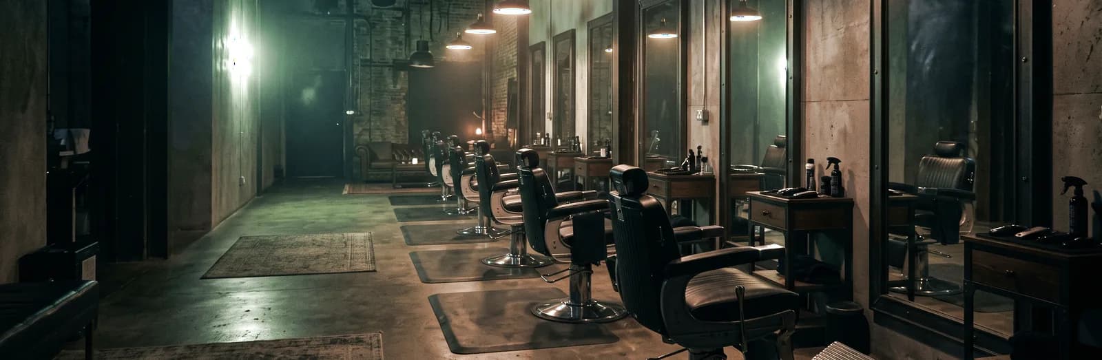 Salão de barbearia em luz baixa, com cadeiras diante dos espelhos. Imagem ilustrativa.